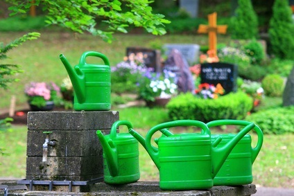Gießkannen stehen an einem Friedhofsbrunnen