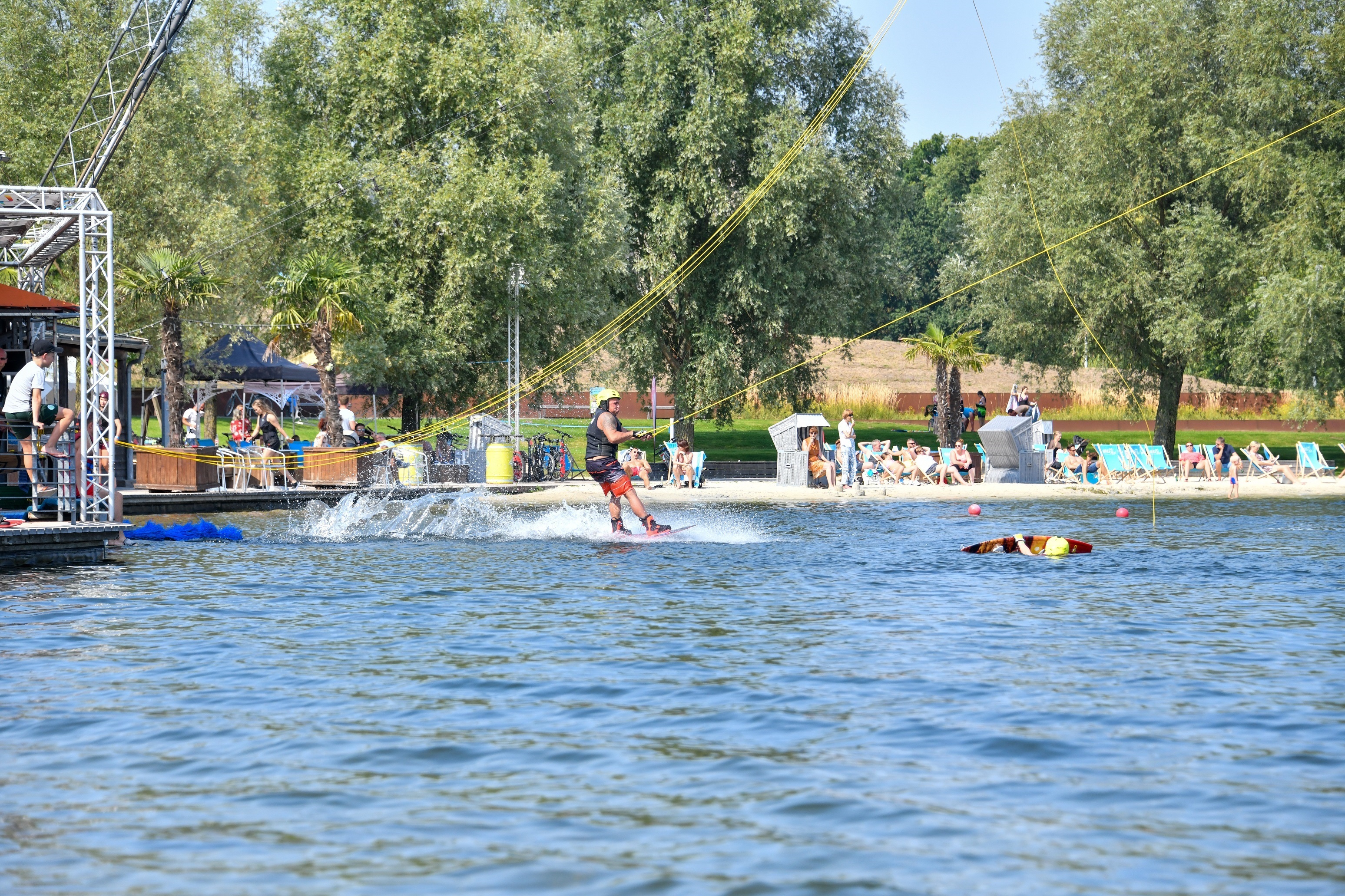 Wakeboarder am Startpunkt, im Hintergrund sitzen Gäste am Strand