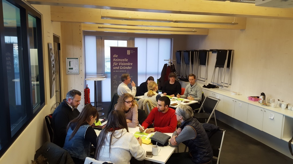 Jugendliche sitzen mit Erwachsenen an Tischen