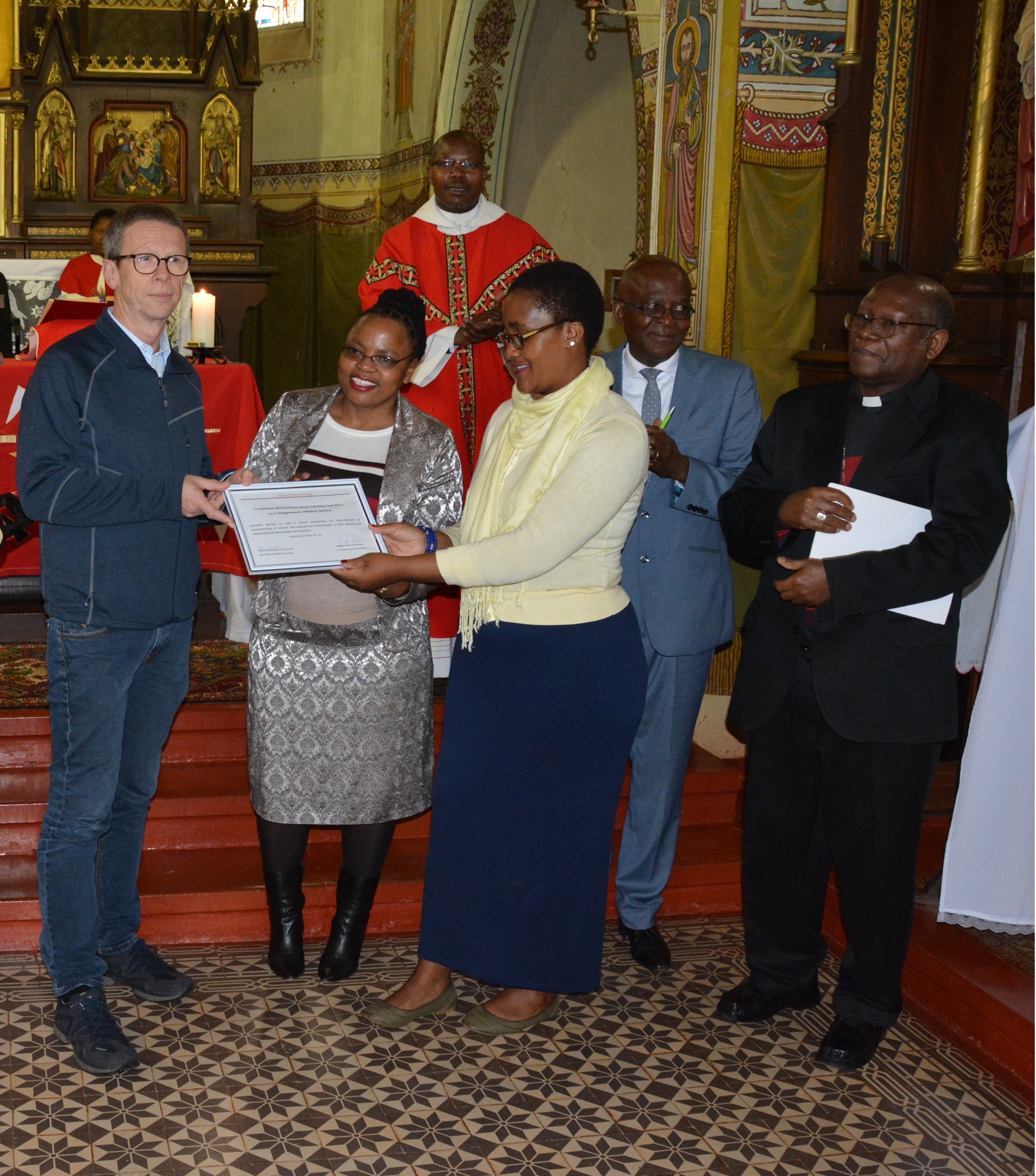 Oberbürgermeister Klaus Mohrs (links) überreicht die Urkunde zur Schulpartnerschaft an Schulleiterin Nombuso Mkhize (3.v.r.) in Anwesenheit von Bischof Pius Mlungisi Dlungwane (rechts)
