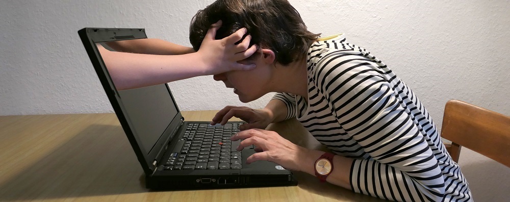 Eine Frau am Laptop und Hände, die aus dem Bildschirm heraus ihren Kopf greifen