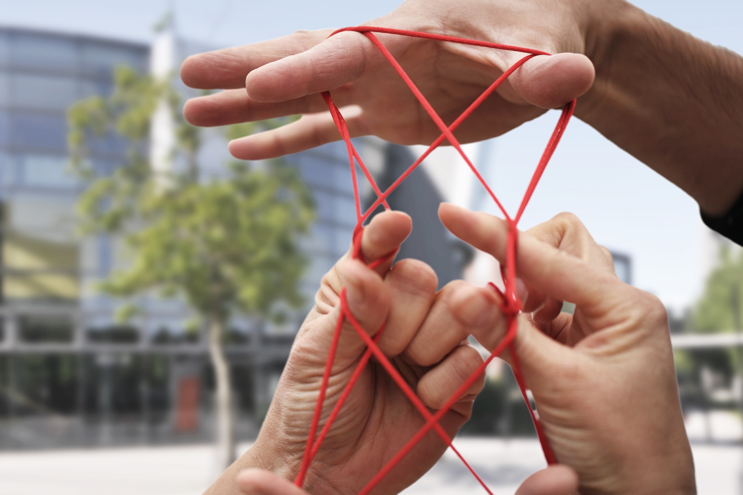 Hände formen ein Netz mit einem roten Faden